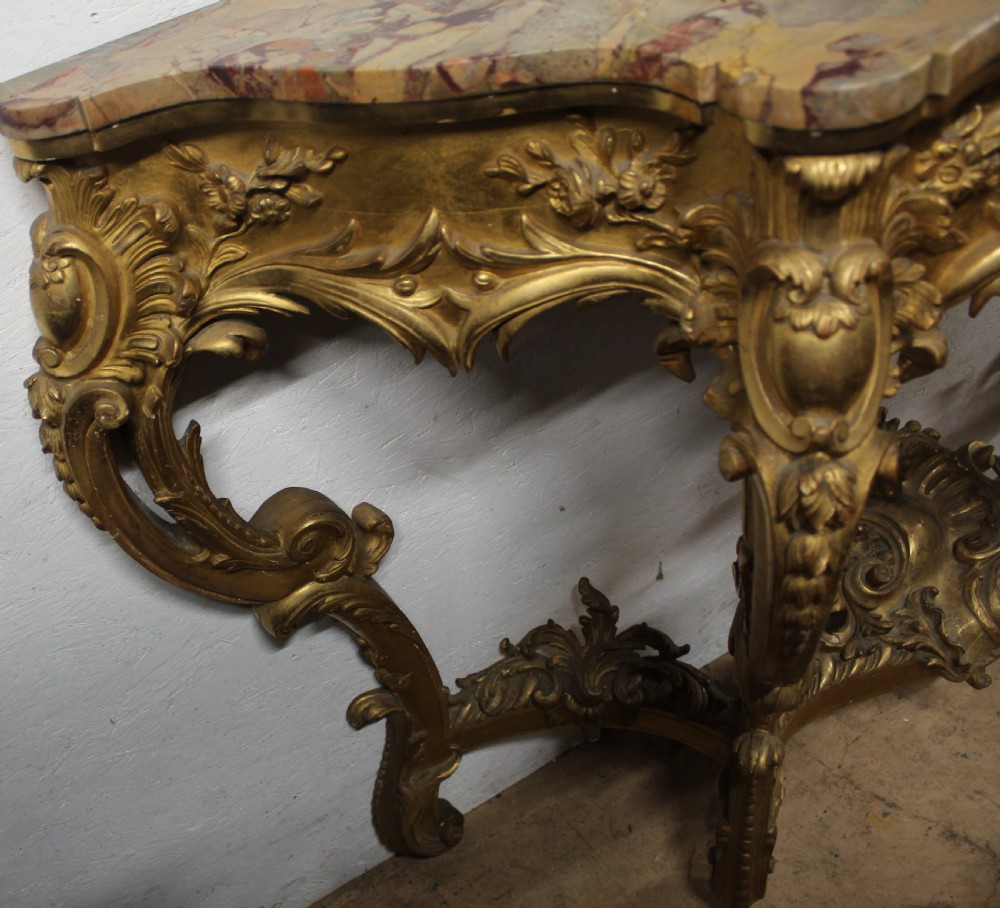 A Rococo style giltwood console table featuring ornate acanthus leaf carving, C-scroll legs, a central shell motif stretcher, and a serpentine variegated marble top. View IV