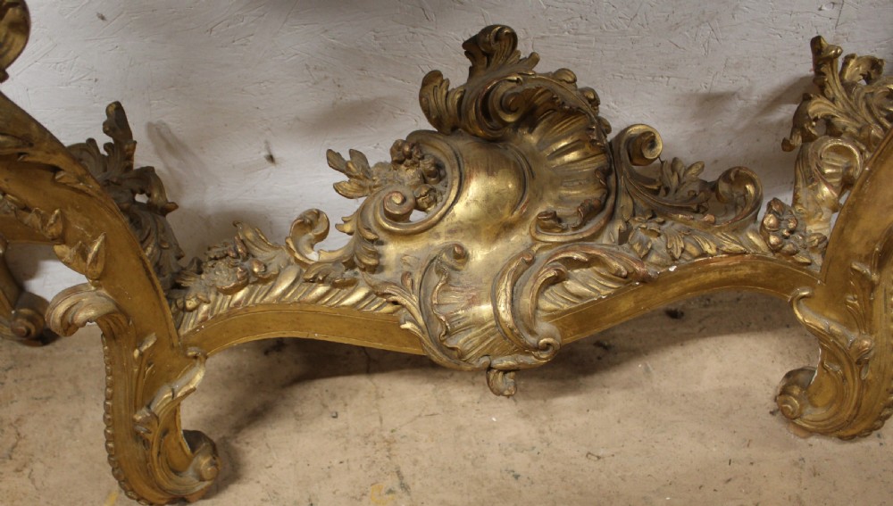 A Rococo style giltwood console table featuring ornate acanthus leaf carving, C-scroll legs, a central shell motif stretcher, and a serpentine variegated marble top. View VI