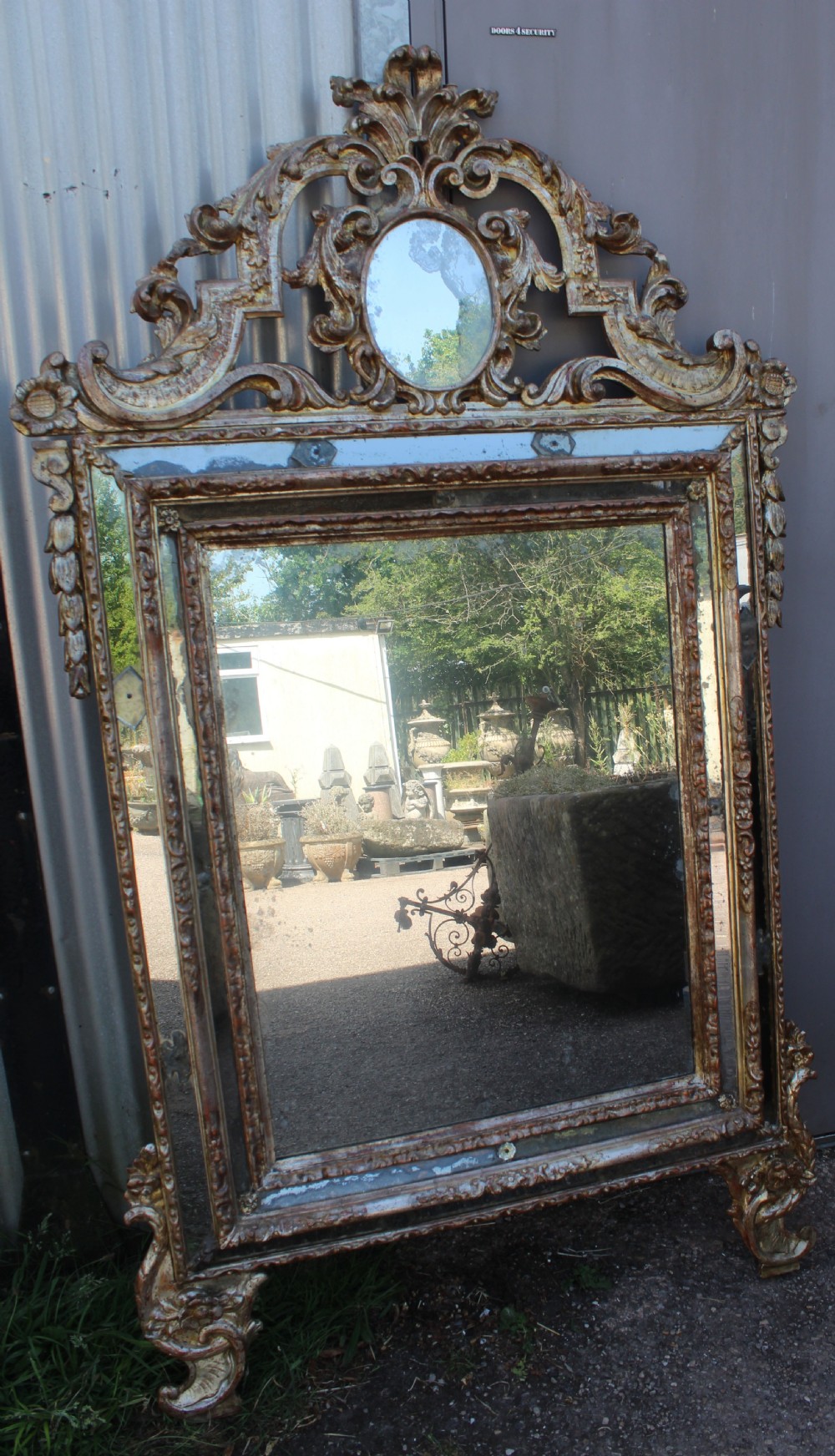 An antique Italian gilded wood mirror featuring a carved ornate crest with a small oval mirror, framed by mirrored glass borders and scroll feet. View II