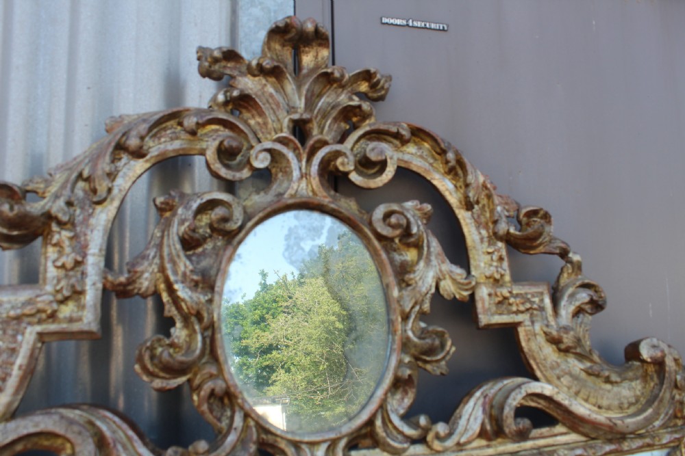 An antique Italian gilded wood mirror featuring a carved ornate crest with a small oval mirror, framed by mirrored glass borders and scroll feet. View IV