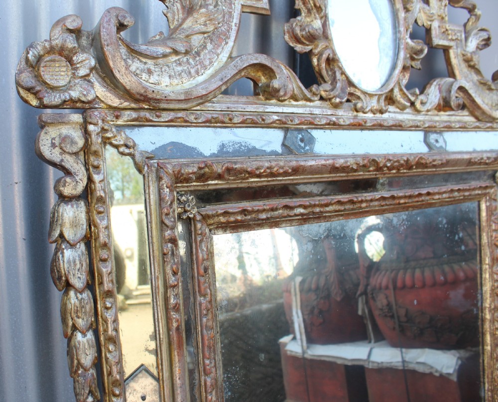 An antique Italian gilded wood mirror featuring a carved ornate crest with a small oval mirror, framed by mirrored glass borders and scroll feet. View V