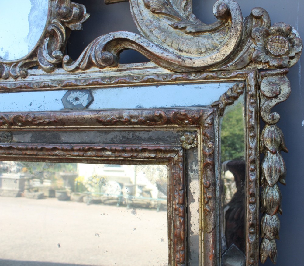 An antique Italian gilded wood mirror featuring a carved ornate crest with a small oval mirror, framed by mirrored glass borders and scroll feet. View VI