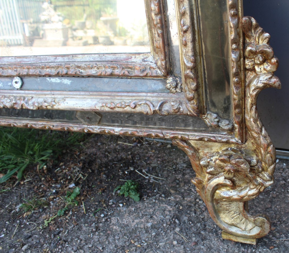 An antique Italian gilded wood mirror featuring a carved ornate crest with a small oval mirror, framed by mirrored glass borders and scroll feet. View VII
