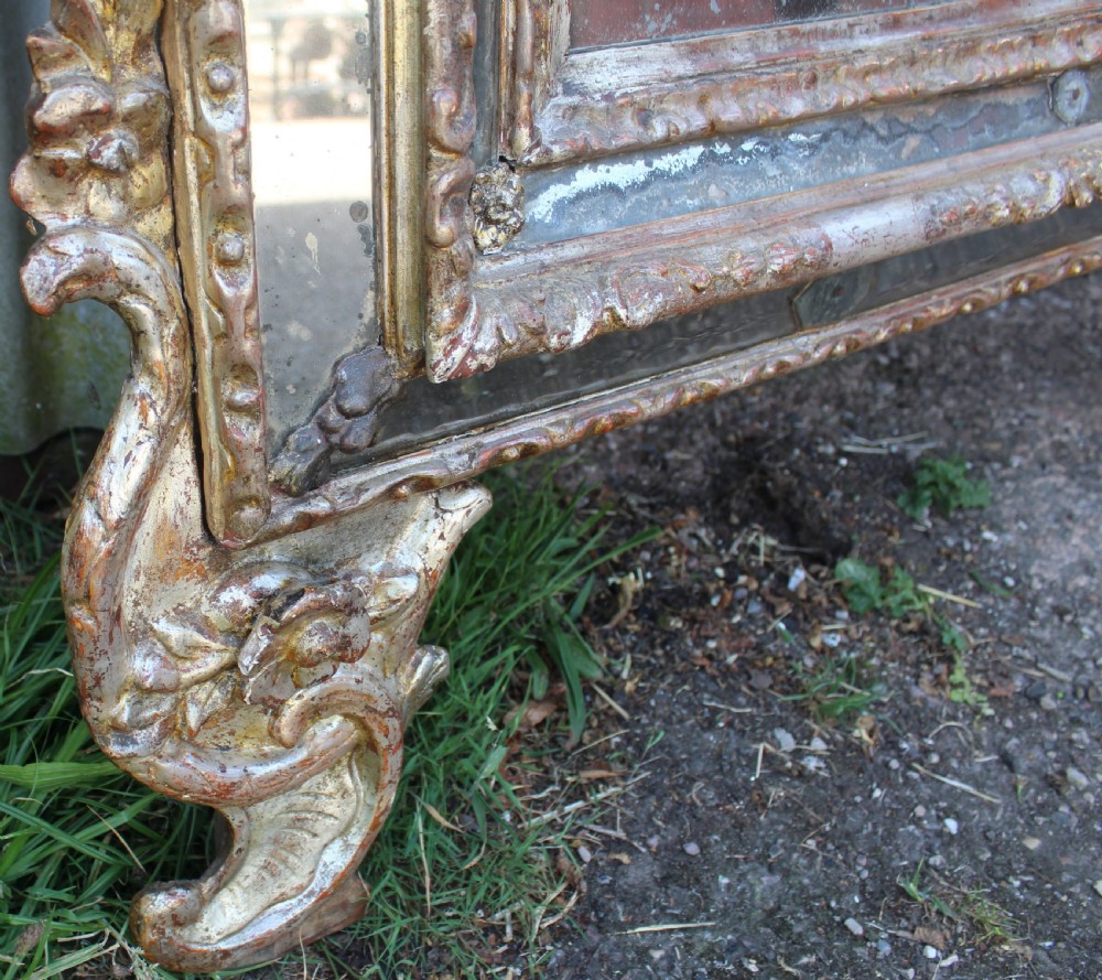 An antique Italian gilded wood mirror featuring a carved ornate crest with a small oval mirror, framed by mirrored glass borders and scroll feet. View VIII