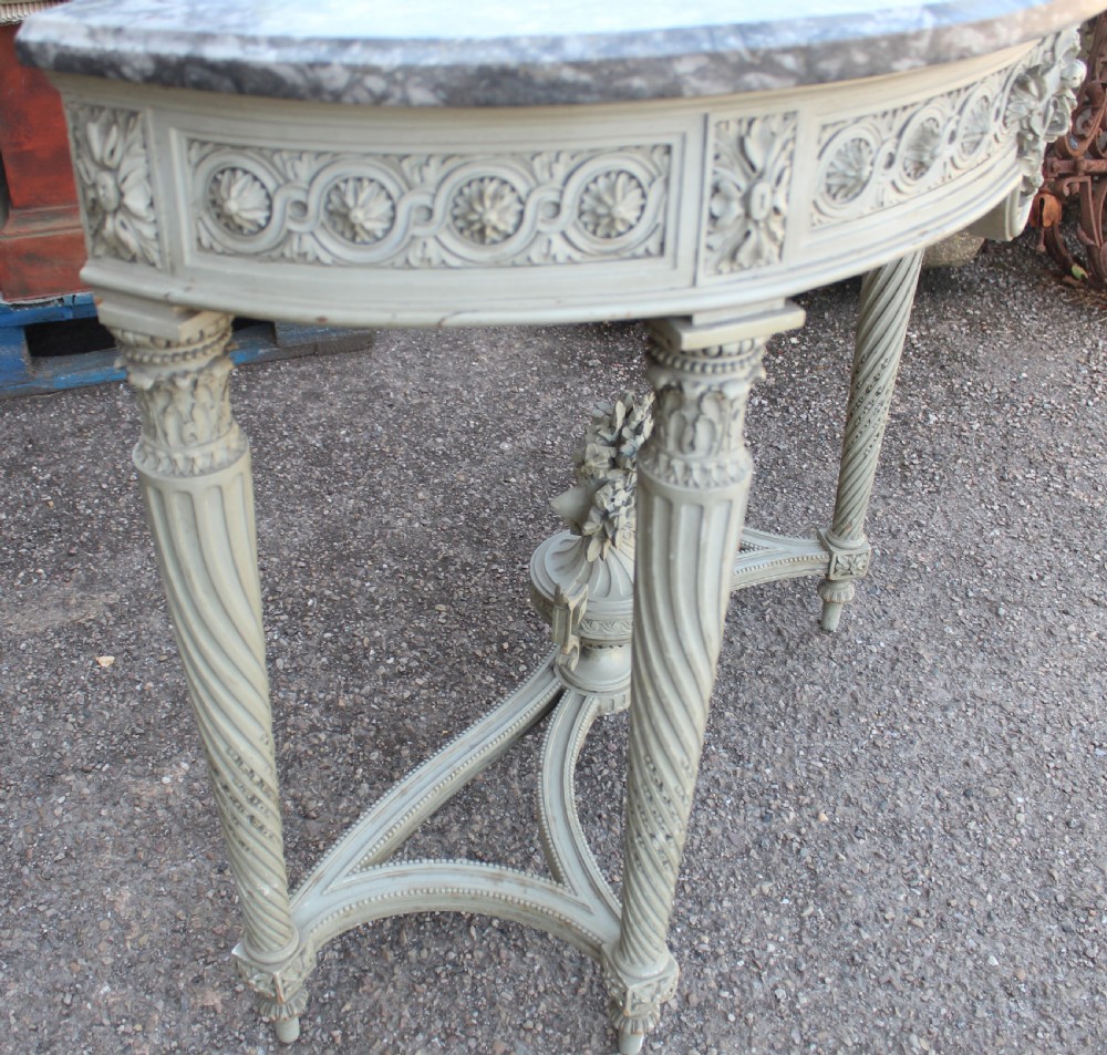 A Neoclassical French Louis XVI style demilune console table featuring a grey marble top, painted off-white carved apron, spiralled fluted legs, and a stretcher centred with a carved urn. View II