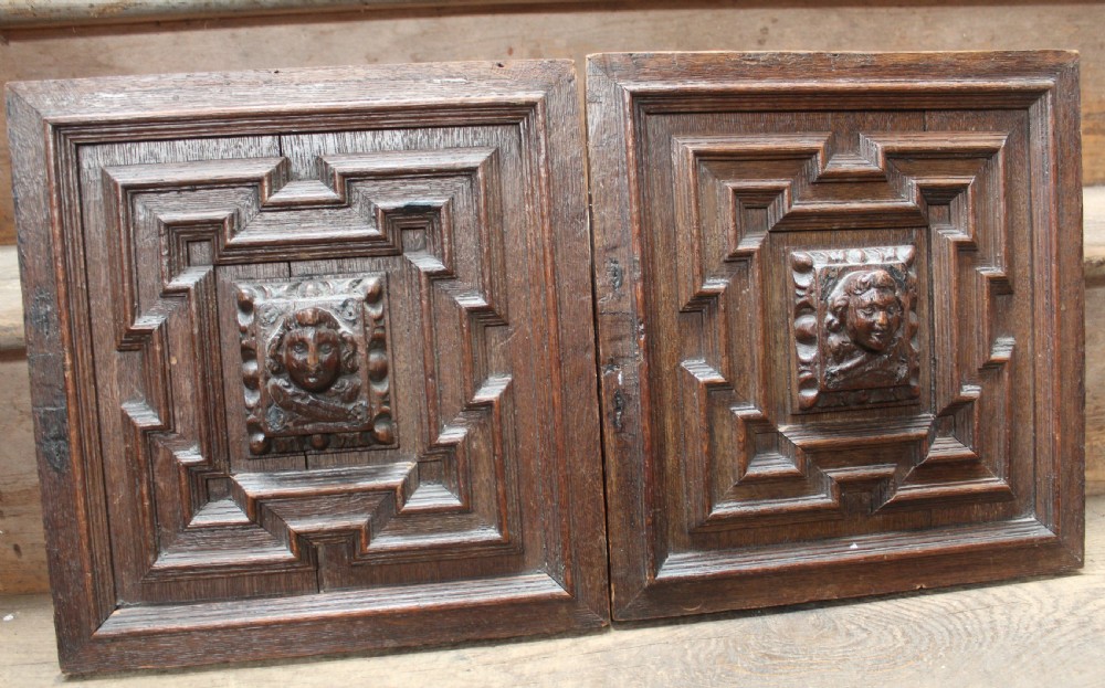 A pair of square dark oak panels featuring raised geometric mouldings surrounding central relief carvings of human faces.