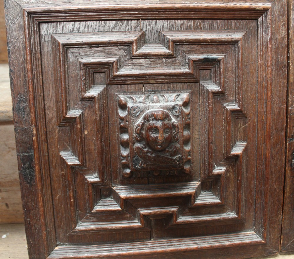 A pair of square dark oak panels featuring raised geometric mouldings surrounding central relief carvings of human faces. View II