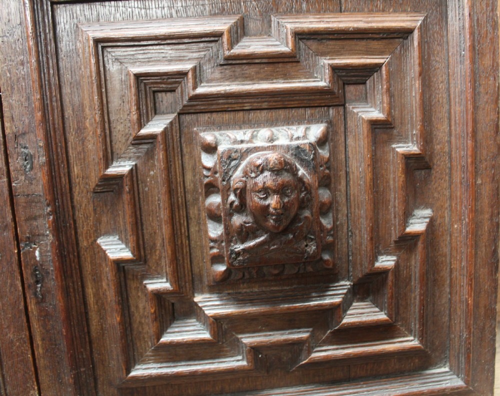 A pair of square dark oak panels featuring raised geometric mouldings surrounding central relief carvings of human faces. View III
