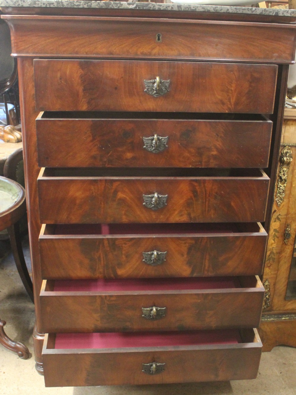 A tall 19th-century French flame mahogany semainier chest of drawers with a fitted grey marble top and ornamental brass handles. View VI