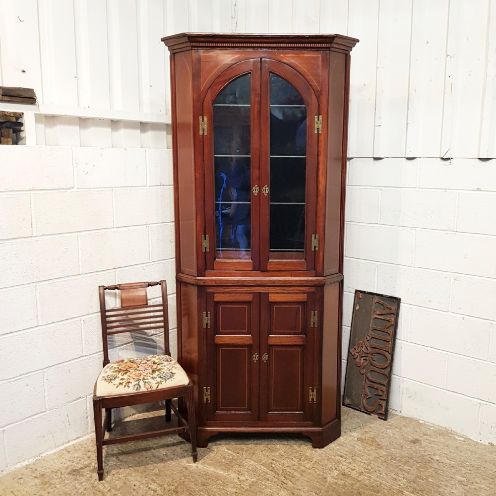 A full height antique Regency mahogany corner cabinet featuring arched glazed upper doors, inlaid lower panel doors, and brass hardware.