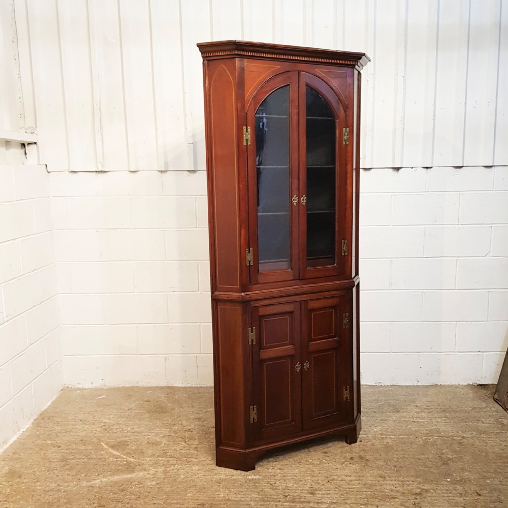 A full height antique Regency mahogany corner cabinet featuring arched glazed upper doors, inlaid lower panel doors, and brass hardware. View II