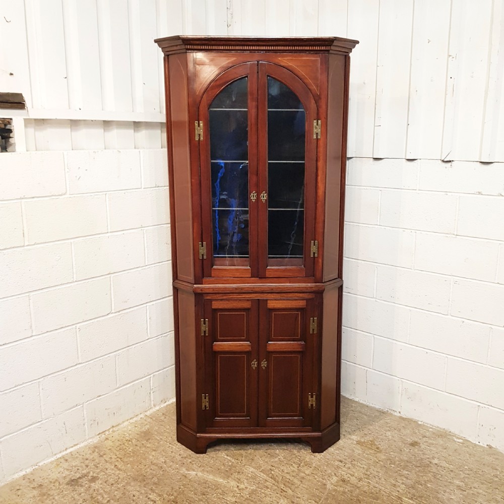 A full height antique Regency mahogany corner cabinet featuring arched glazed upper doors, inlaid lower panel doors, and brass hardware. View III