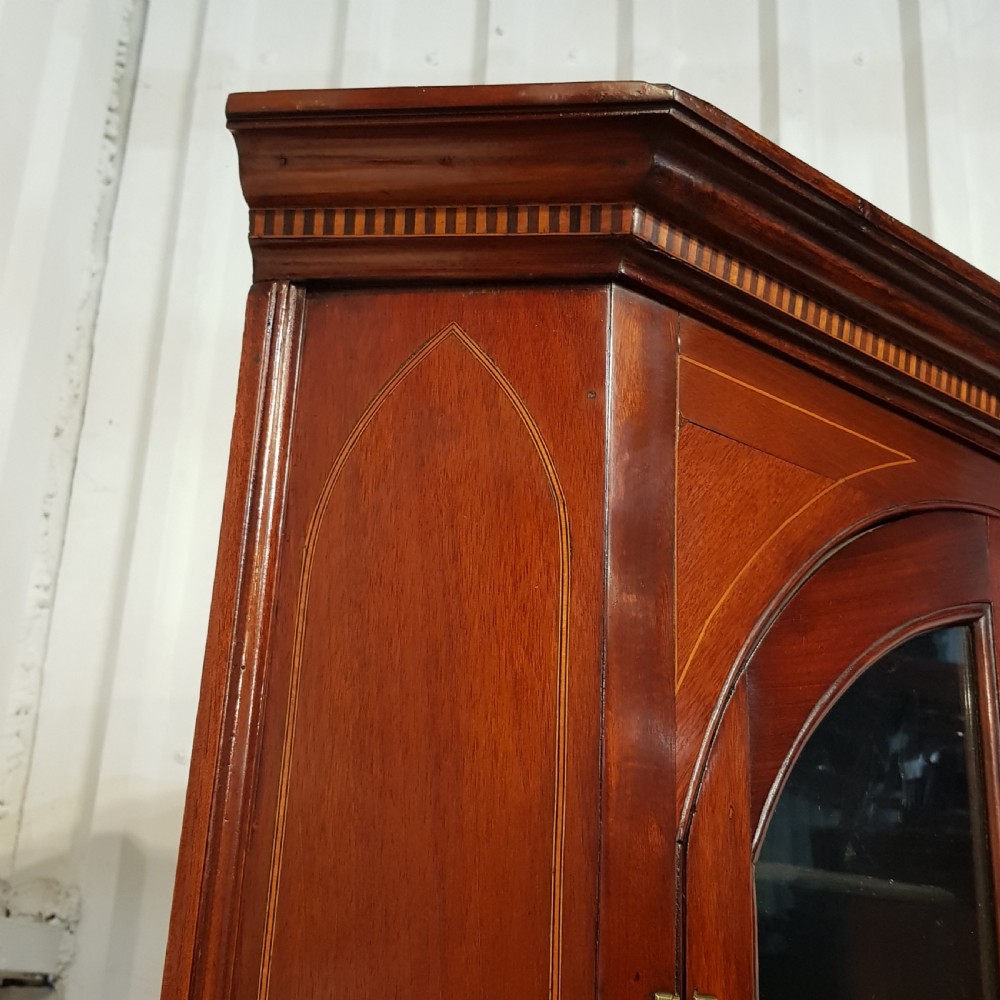 A full height antique Regency mahogany corner cabinet featuring arched glazed upper doors, inlaid lower panel doors, and brass hardware. View V