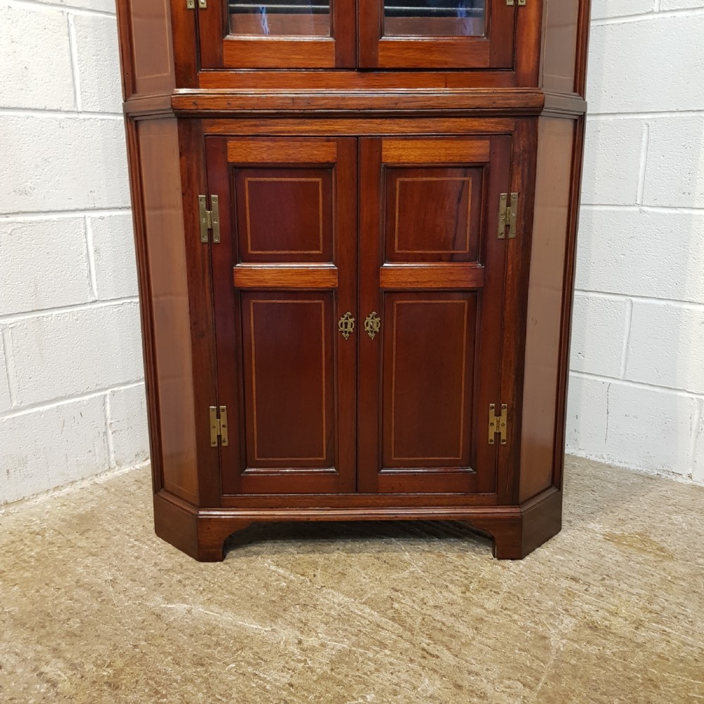 A full height antique Regency mahogany corner cabinet featuring arched glazed upper doors, inlaid lower panel doors, and brass hardware. View VI