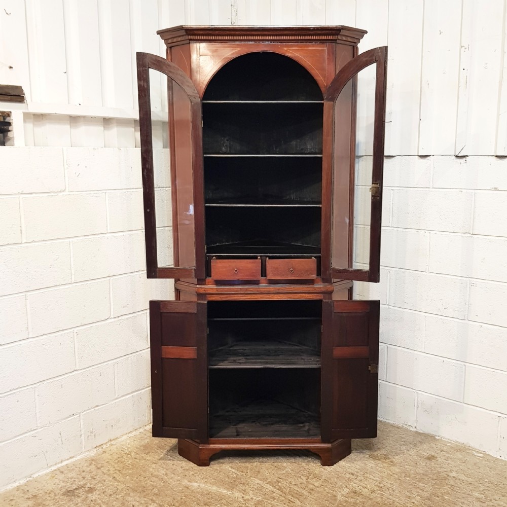 A full height antique Regency mahogany corner cabinet featuring arched glazed upper doors, inlaid lower panel doors, and brass hardware. View VII