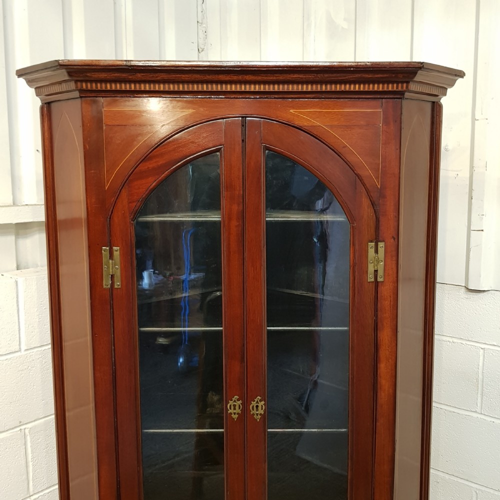 A full height antique Regency mahogany corner cabinet featuring arched glazed upper doors, inlaid lower panel doors, and brass hardware. View VIII