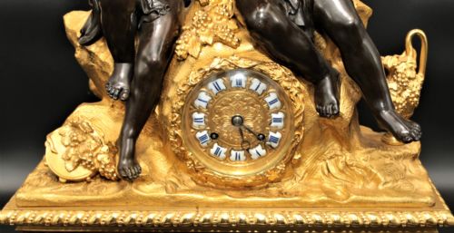 fig 2. An antique French mantel clock featuring dark bronze figures of two winged cherubs atop a gilded bronze mount and red marble base.