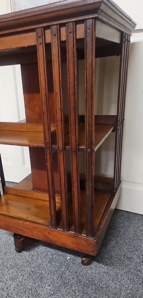 An Edwardian mahogany revolving bookcase featuring vertical slatted sides, two tiers of open shelving, and a square moulded top set on a rotating cross base. View III