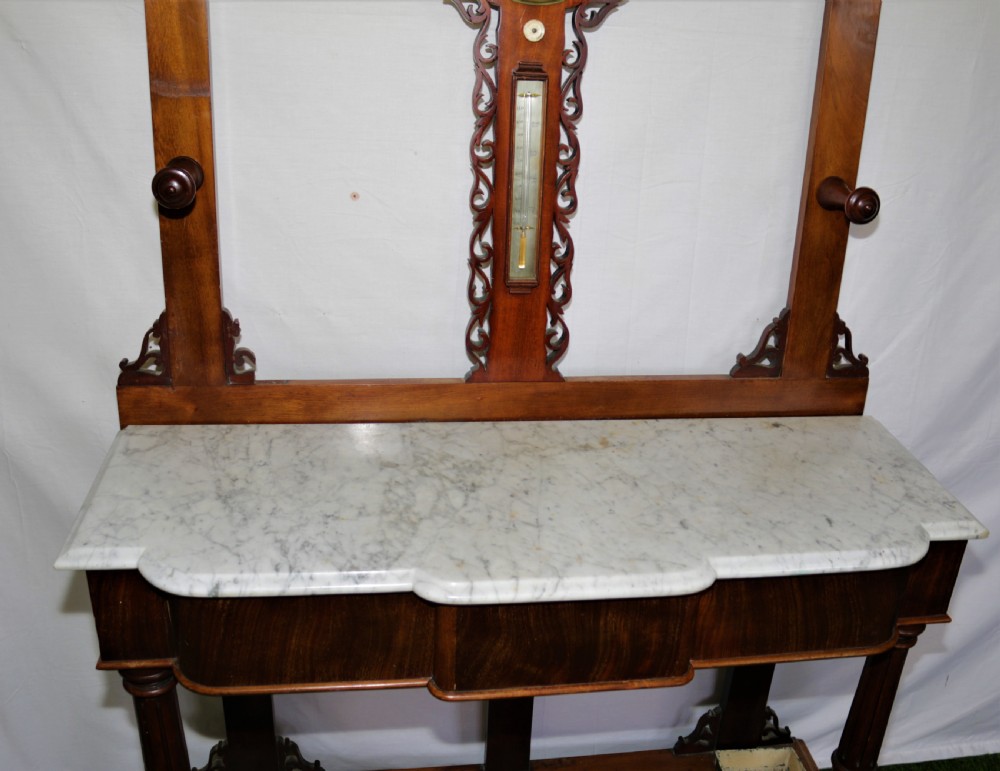 A Victorian mahogany hall stand featuring turned pegs, fretwork carving, an integrated barometer and thermometer, a white marble console surface, and lower drip trays. View III