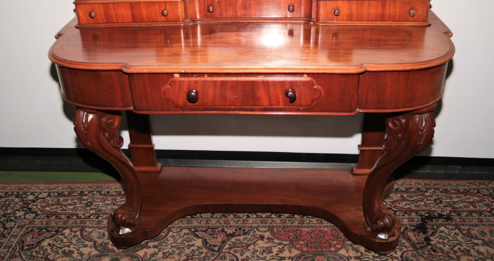 A Victorian flame mahogany Duchess dressing table featuring an oval swivel mirror, upper trinket drawers, and carved scroll legs. View V