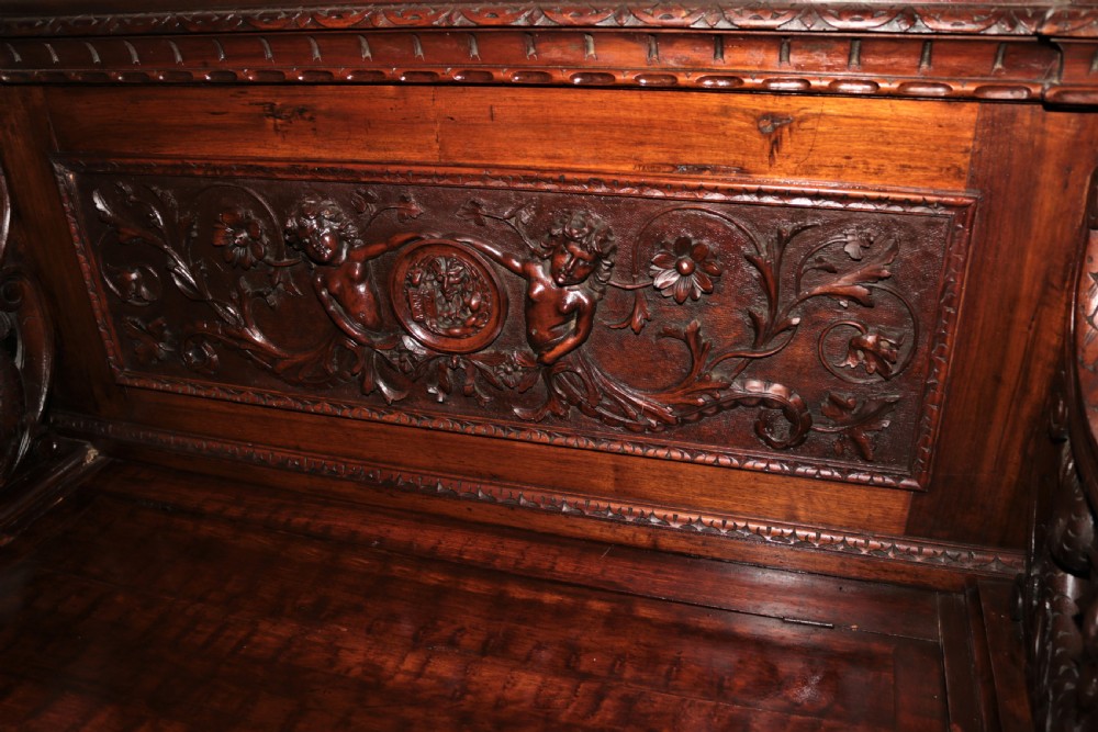 A dark carved walnut hall seat featuring high-relief carvings of mythical figures and floral scrollwork on the backrest and front storage panel. View II