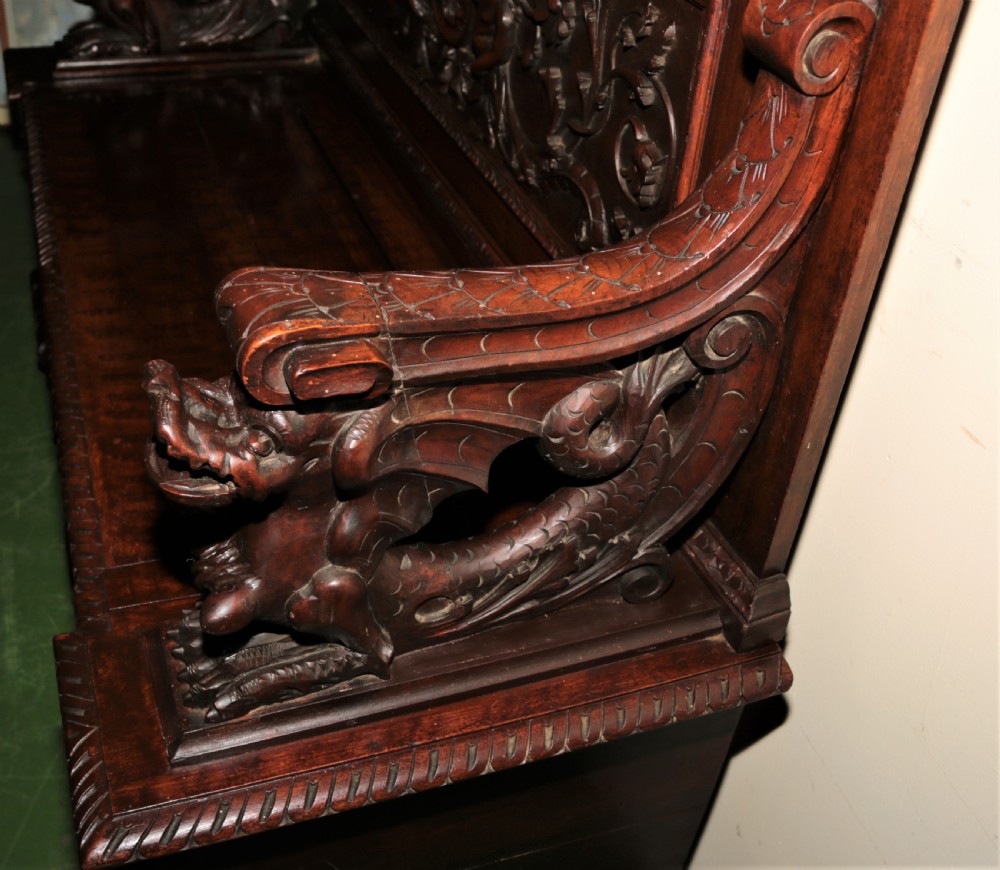 A dark carved walnut hall seat featuring high-relief carvings of mythical figures and floral scrollwork on the backrest and front storage panel. View III