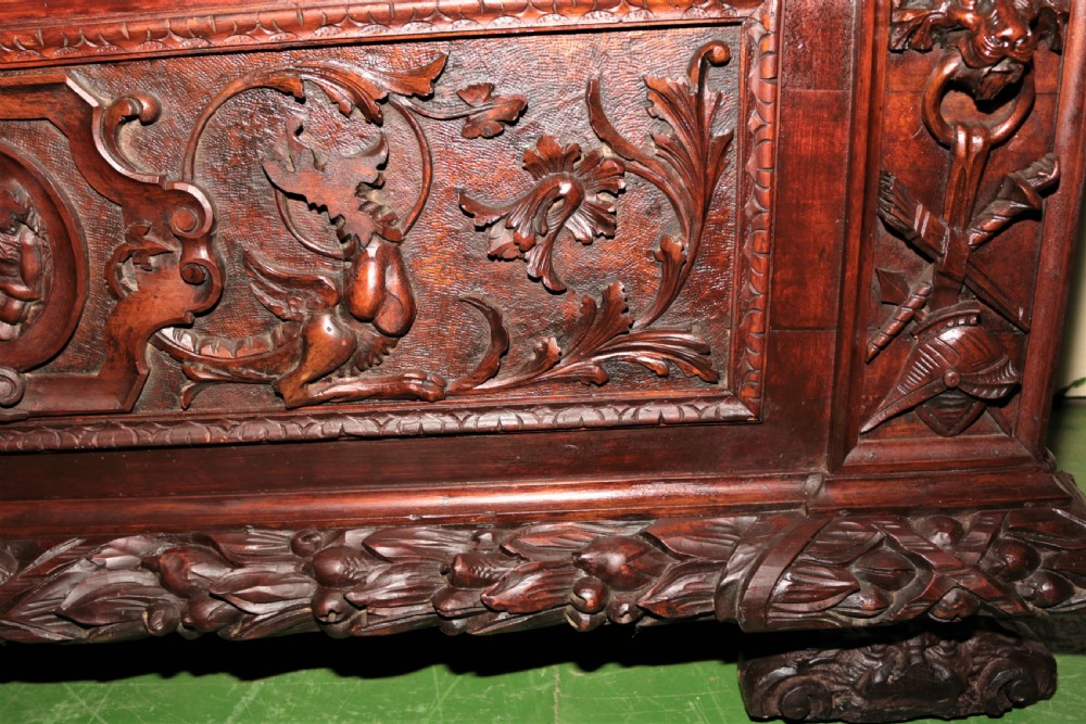 A dark carved walnut hall seat featuring high-relief carvings of mythical figures and floral scrollwork on the backrest and front storage panel. View V