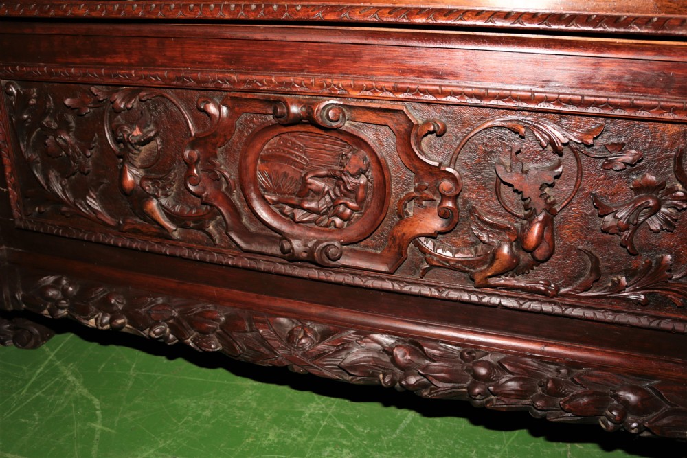 A dark carved walnut hall seat featuring high-relief carvings of mythical figures and floral scrollwork on the backrest and front storage panel. View VI