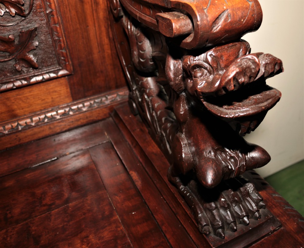 A dark carved walnut hall seat featuring high-relief carvings of mythical figures and floral scrollwork on the backrest and front storage panel. View VII