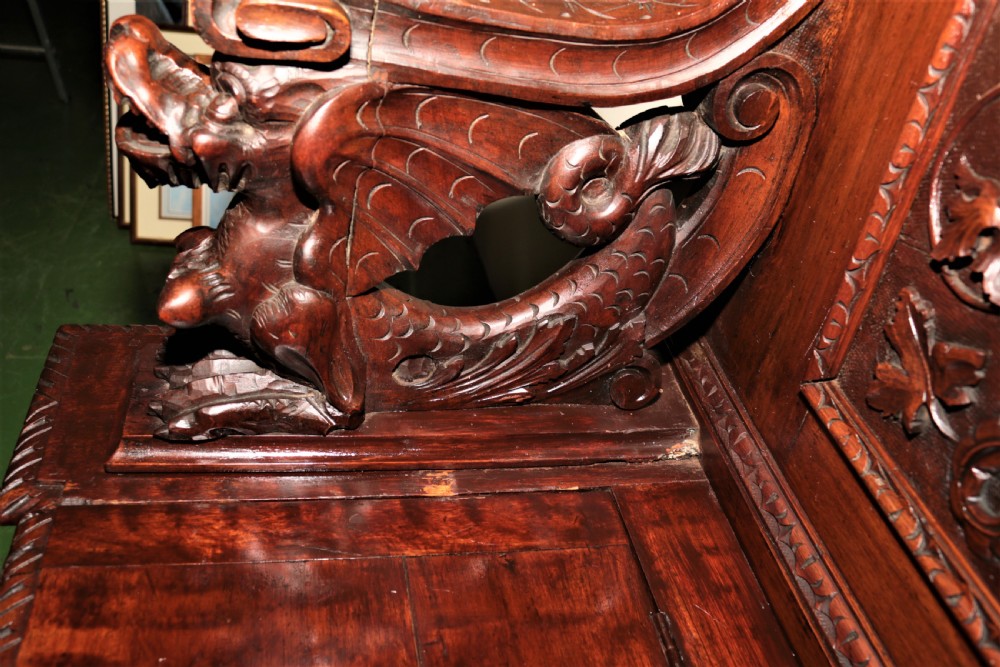 A dark carved walnut hall seat featuring high-relief carvings of mythical figures and floral scrollwork on the backrest and front storage panel. View XI