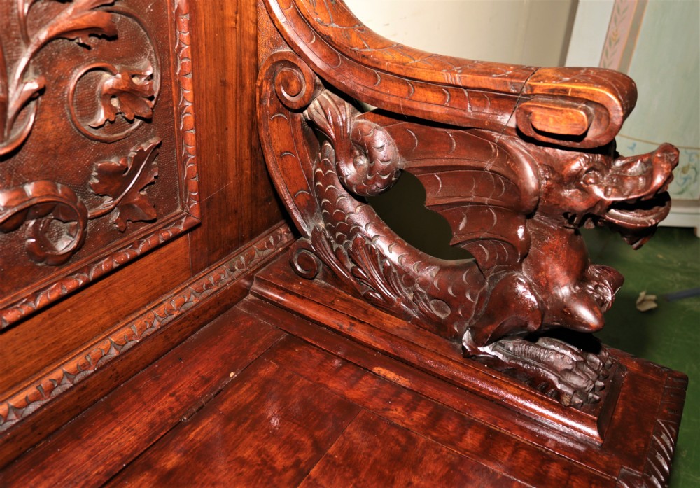 A dark carved walnut hall seat featuring high-relief carvings of mythical figures and floral scrollwork on the backrest and front storage panel. View XII