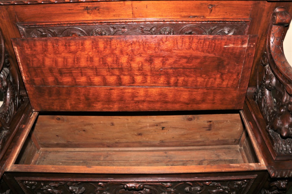 A dark carved walnut hall seat featuring high-relief carvings of mythical figures and floral scrollwork on the backrest and front storage panel. View XIII
