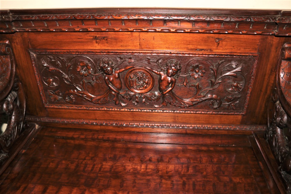 A dark carved walnut hall seat featuring high-relief carvings of mythical figures and floral scrollwork on the backrest and front storage panel. View XV