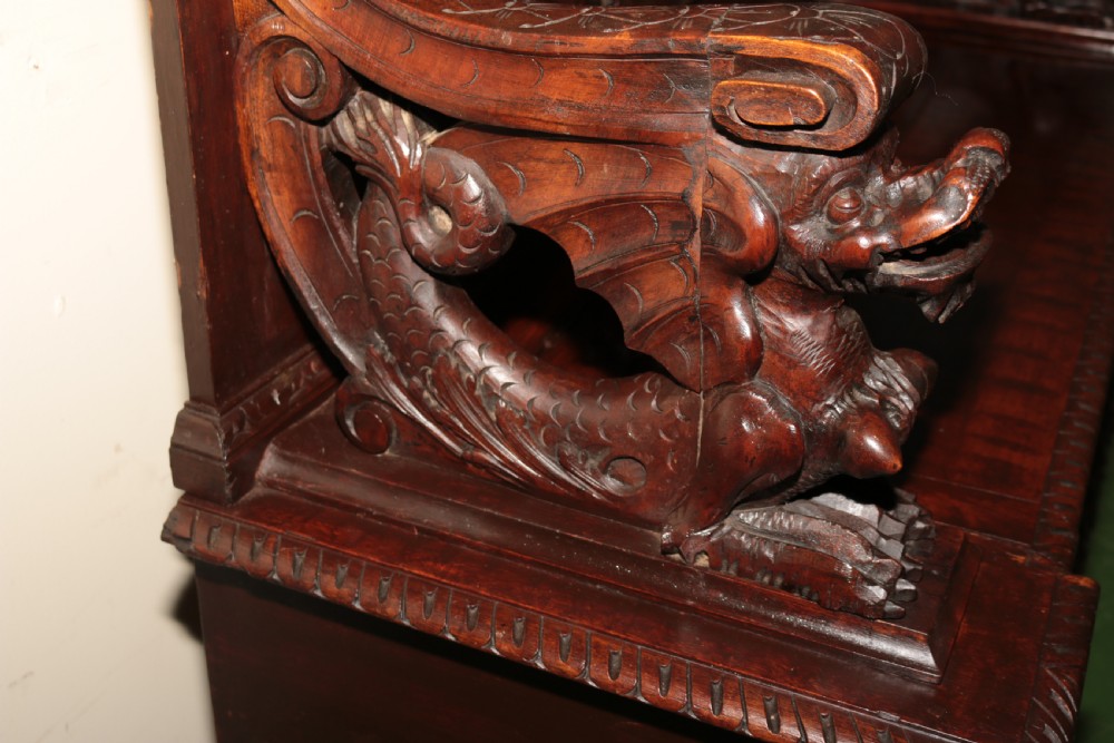 A dark carved walnut hall seat featuring high-relief carvings of mythical figures and floral scrollwork on the backrest and front storage panel. View XIX