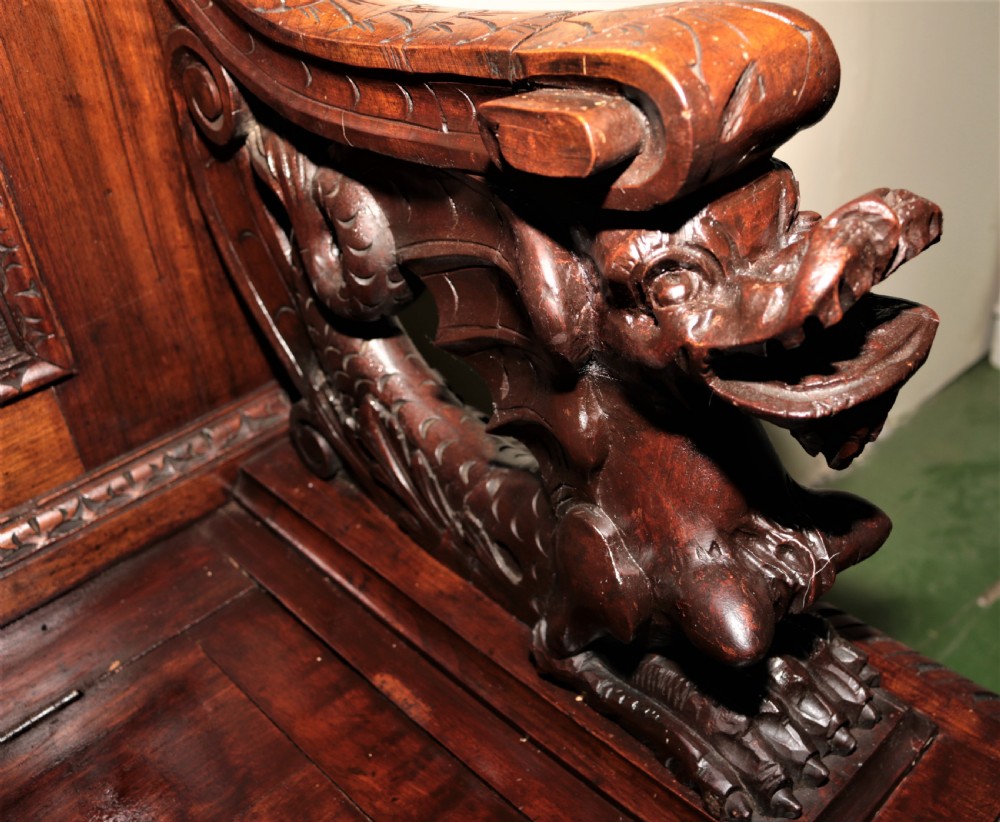 A dark carved walnut hall seat featuring high-relief carvings of mythical figures and floral scrollwork on the backrest and front storage panel. View XXIII
