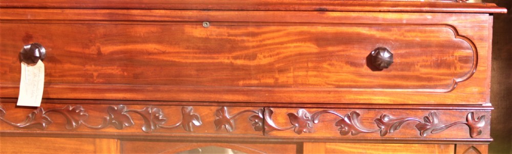 A William IV flame mahogany secretaire bookcase featuring twin arch glazed upper doors topped with a carved central finial, above a long drawer and lower cabinet section. View III