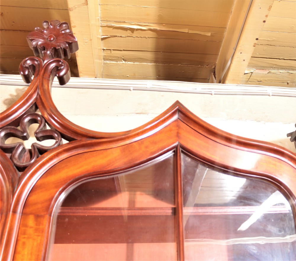 A William IV flame mahogany secretaire bookcase featuring twin arch glazed upper doors topped with a carved central finial, above a long drawer and lower cabinet section. View IX