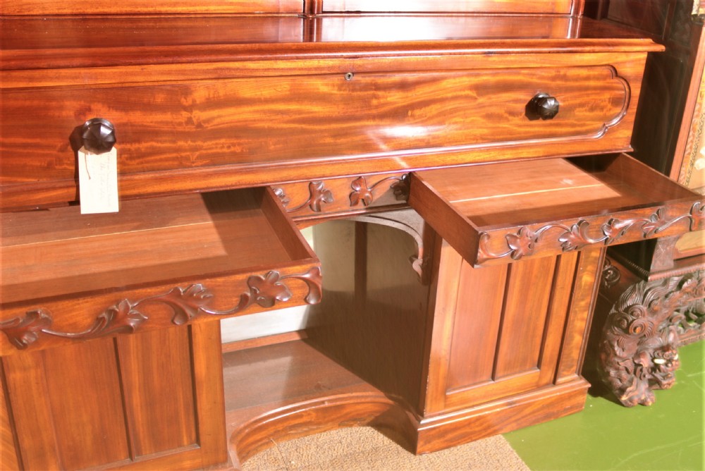 A William IV flame mahogany secretaire bookcase featuring twin arch glazed upper doors topped with a carved central finial, above a long drawer and lower cabinet section. View X