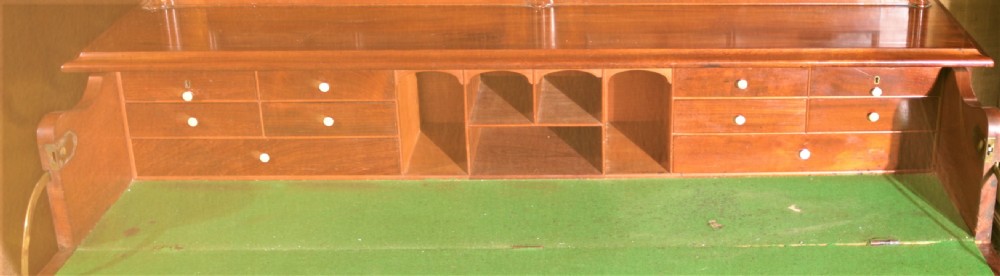 A William IV flame mahogany secretaire bookcase featuring twin arch glazed upper doors topped with a carved central finial, above a long drawer and lower cabinet section. View XII