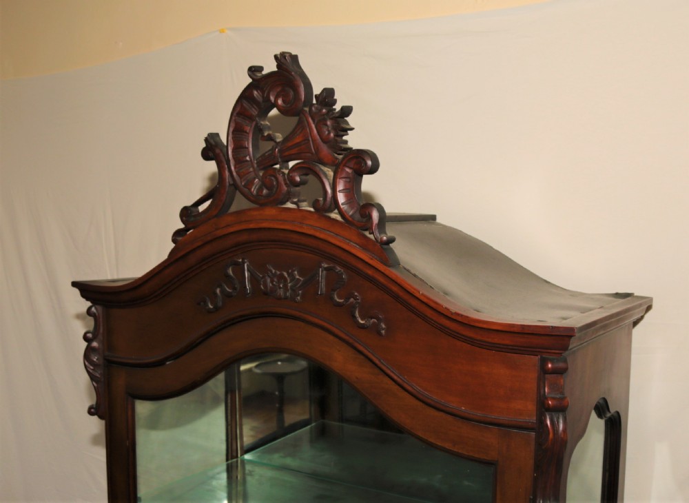 A dark brown carved mahogany display cabinet featuring glass doors and side panels, interior glass shelves, an ornate carved crest, and slender cabriole legs. View IX