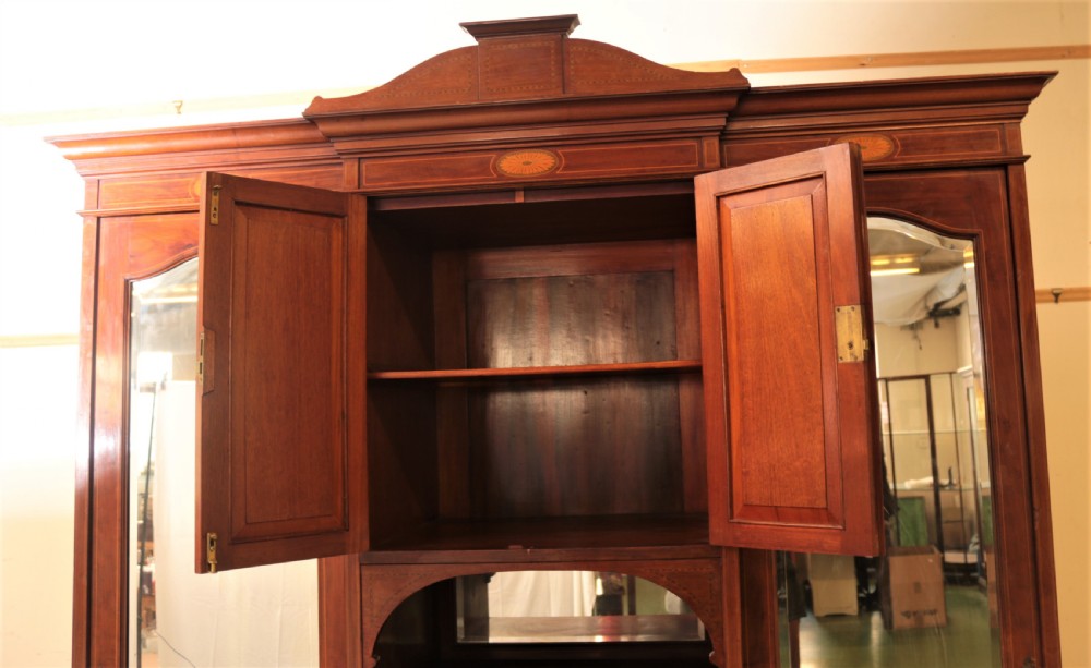 An Edwardian mahogany combination wardrobe with two outer mirrored doors, a central cupboard featuring oval satinwood inlay, an open niche, and lower drawers. View V