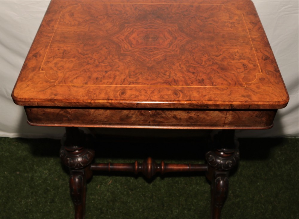A Victorian burr walnut sewing table featuring a rectangular inlaid top, a hanging wooden work well, turned side supports, and carved legs on castors. View II