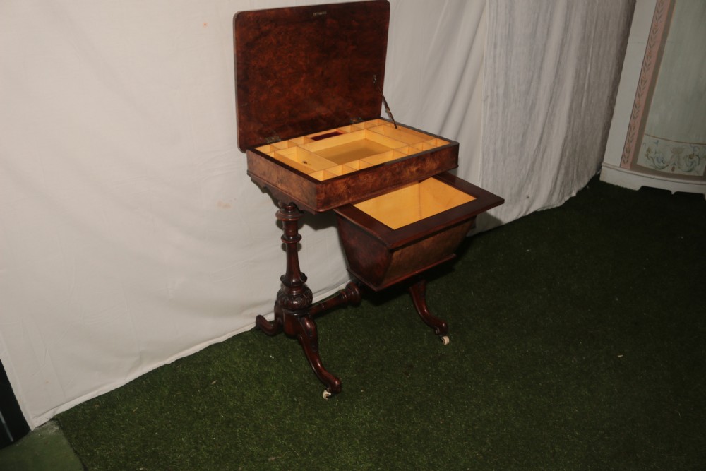 A Victorian burr walnut sewing table featuring a rectangular inlaid top, a hanging wooden work well, turned side supports, and carved legs on castors. View VII