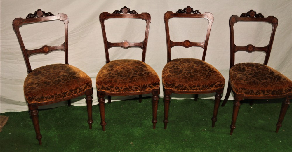 A set of four Victorian walnut side chairs featuring carved crest rails, floral marquetry inlays on the backrest, patterned brown upholstered seats, and turned front legs.