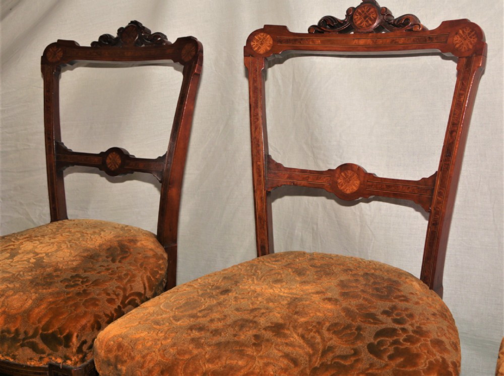 A set of four Victorian walnut side chairs featuring carved crest rails, floral marquetry inlays on the backrest, patterned brown upholstered seats, and turned front legs. View III
