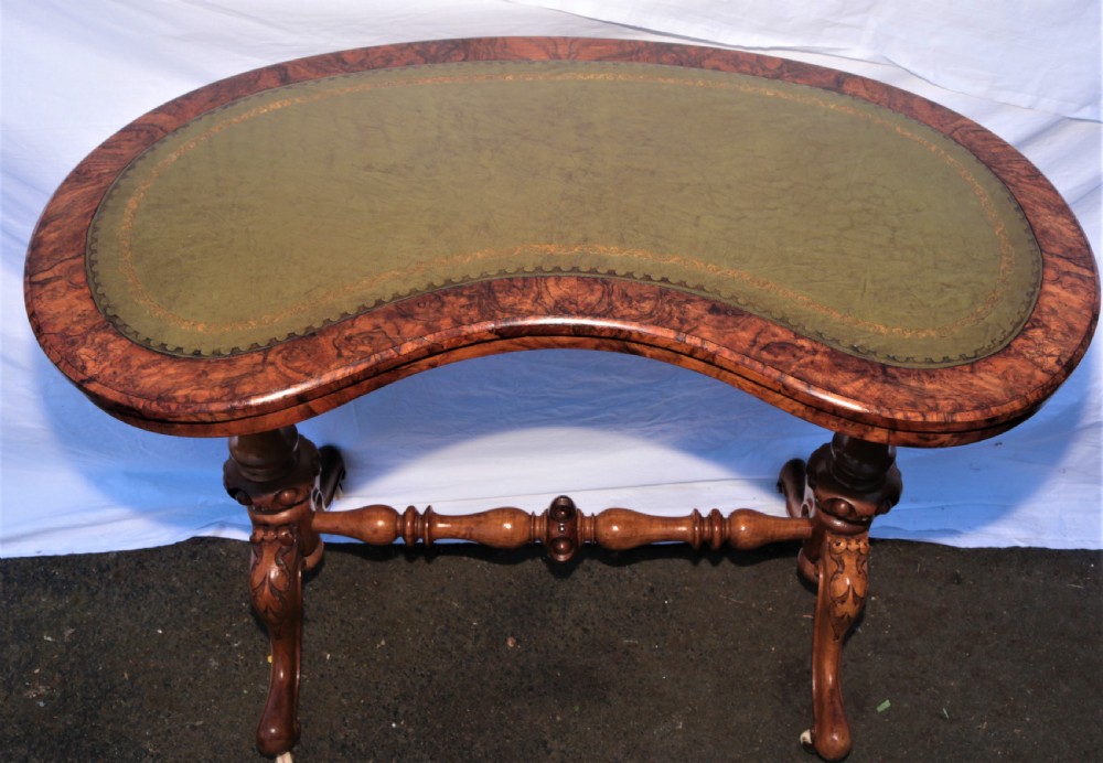 An antique kidney-shaped writing desk crafted from burr walnut with an inset green leather top, carved legs, and a central turned stretcher.