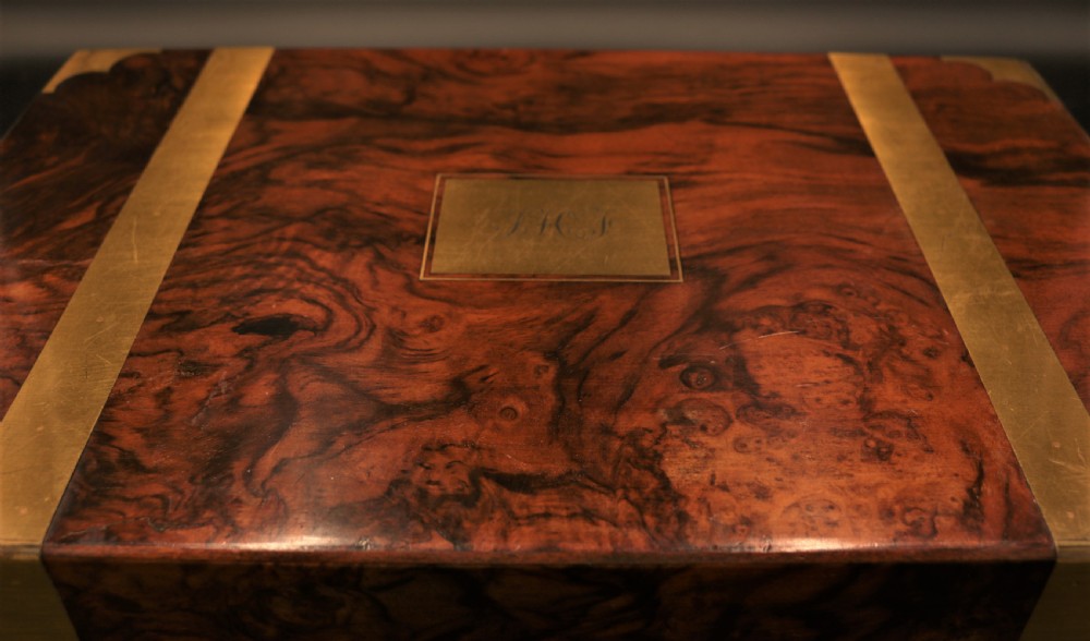 A rectangular Victorian burr walnut writing box featuring brass straps, corner mounts, an engraved central cartouche, and an escutcheon keyhole. View V