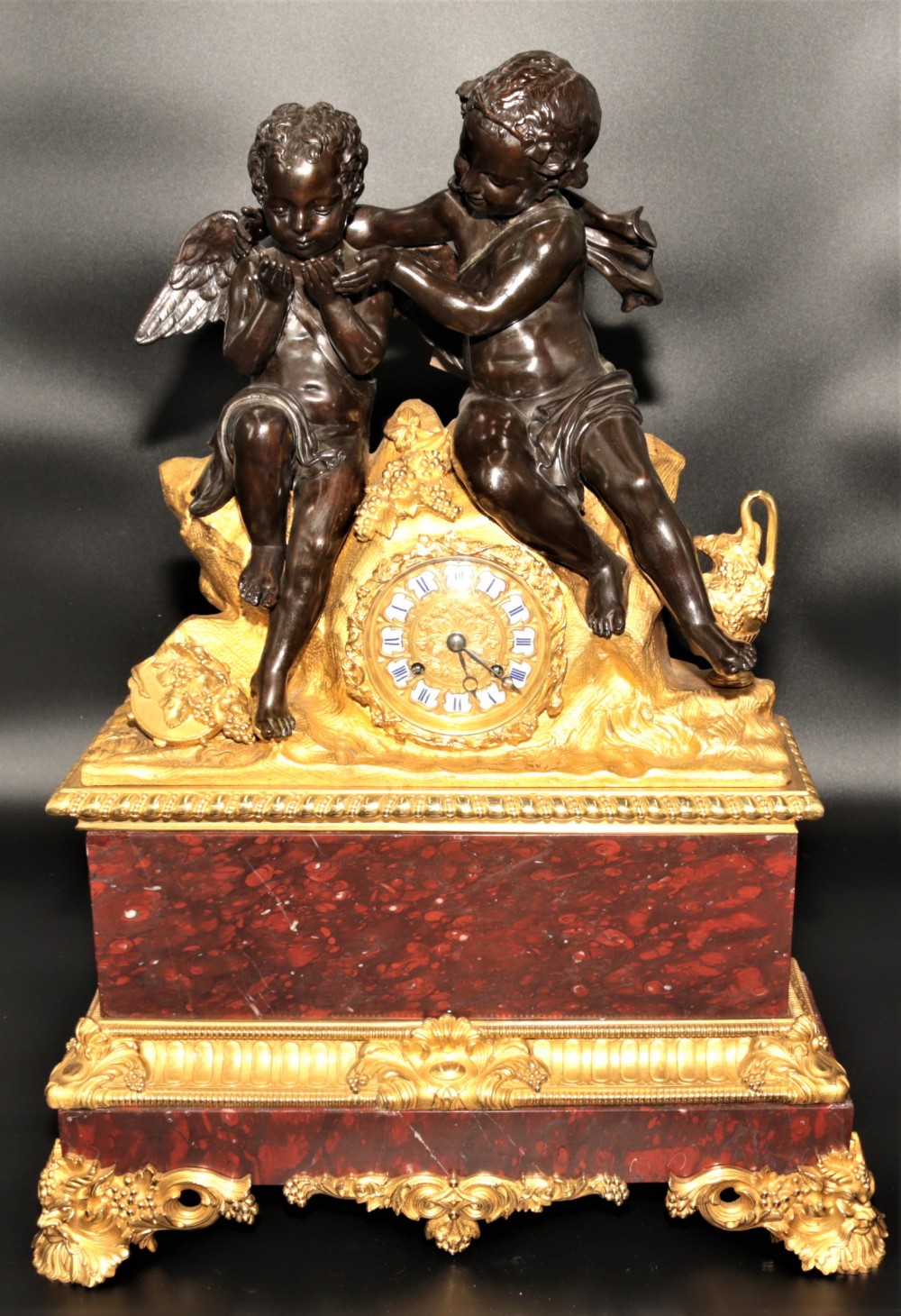 An antique French mantel clock featuring dark bronze figures of two winged cherubs atop a gilded bronze mount and red marble base.