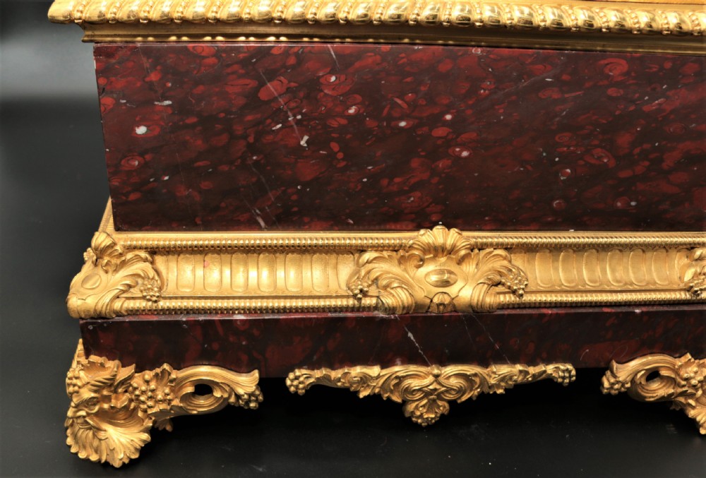 An antique French mantel clock featuring dark bronze figures of two winged cherubs atop a gilded bronze mount and red marble base. View V