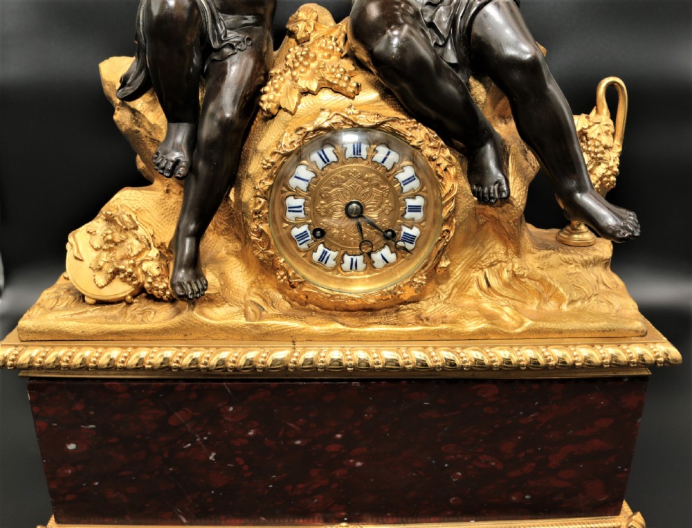 An antique French mantel clock featuring dark bronze figures of two winged cherubs atop a gilded bronze mount and red marble base. View VI